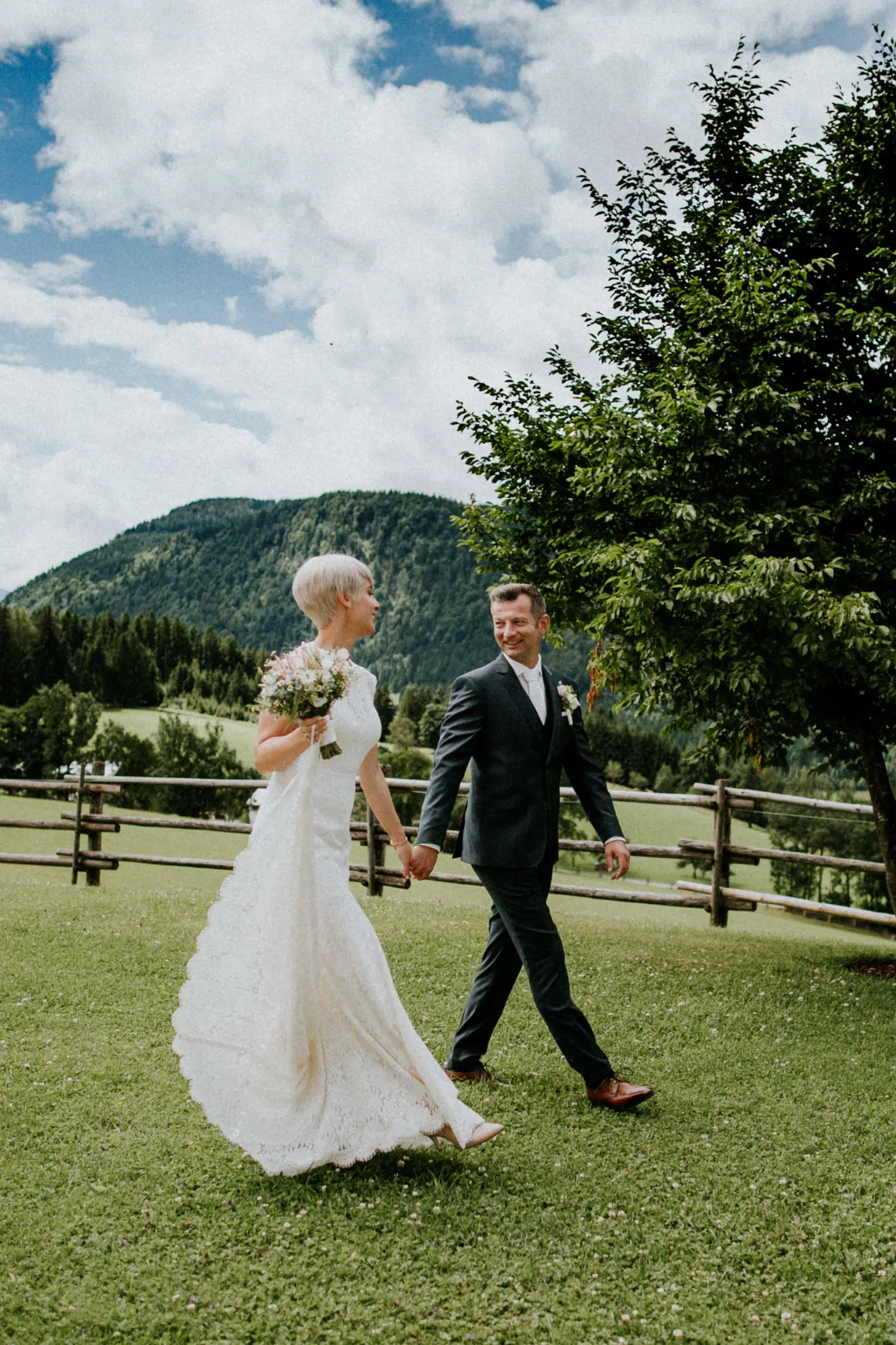 Brautpaarshooting am Winterstellgut. Brautpaar spaziert im Garten vom Winterstellgut, im Hintergrund die Berge und ein tolles Wolkenpannorama.